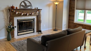 A living room with a fireplace, a floor lamp, and a large window with a view of the outdoors. - Home in quiet friendly neighborhood near the river, parks and walking trails (Wisconsin Rapids)