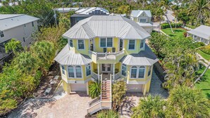 A large, multi-story house with a central balcony, surrounded by lush greenery and a view of the ocean. - Game Room, Pool, Hot Tub, Walk to Beach | Captiva 5BDR | Coco Mango by AvantStay (Captiva)
