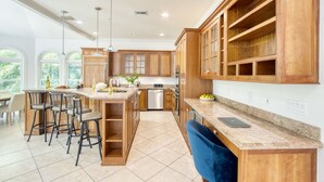 A spacious kitchen with wooden cabinets, a central island with bar stools, a dishwasher, and a laptop on the counter. - Game Room, Pool, Hot Tub, Walk to Beach | Captiva 5BDR | Coco Mango by AvantStay (Captiva)