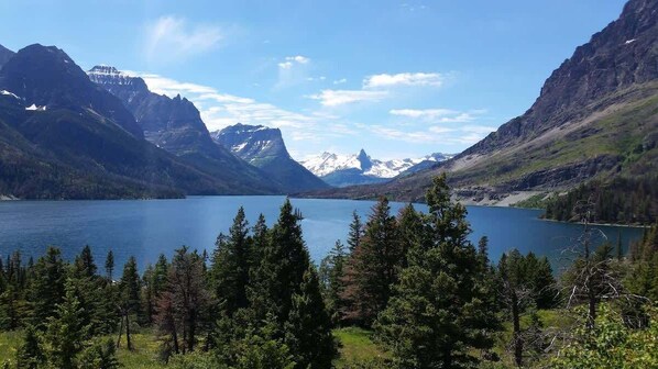 A mountainous landscape with a lake, dense forest, and snow-capped peaks.