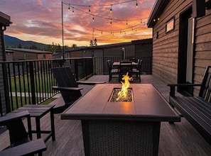 A patio with a fire feature, outdoor seating, and a view of the sunset. - EV Charger | Amazing Views | Pool & Hot Tub (Whitefish)