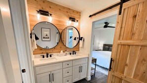 Casa de banho com duas pias, um painel de parede em madeira e uma porta deslizante para um quarto.