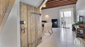 A spacious room with a wooden door, a black sofa, a white rocking chair, and a dining table with a plant. - La Maison aux Portes des Ecluses (HEDE BAZOUGES)
