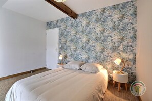 Ein Schlafzimmer mit blumigem Wandpapier, einem Bett mit weißen Leinen, zwei Nachttischen mit Lampen und einer Tür.