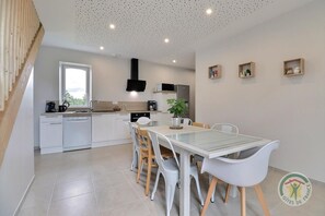 A modern kitchen with white cabinets, a dining table with chairs, and a staircase on the left.