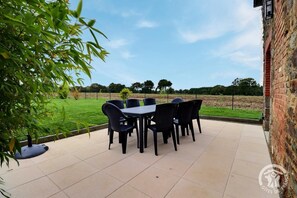 Eine Terrasse im Freien mit Tisch und Stühlen, einer Ziegelwand und einem grasbewachsen Feld im Hintergrund.