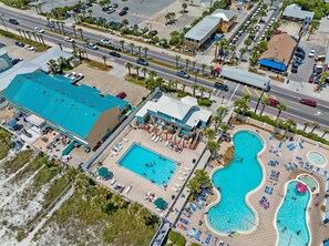 An aerial view of a resort with multiple swimming pools, a beach area, and a parking lot.