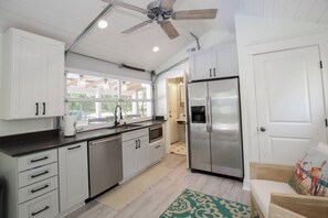 Una cocina moderna con armarios blancos, electrodomésticos de acero inoxidable y un ventilador de techo.