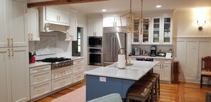 Cocina moderna con muebles blancos, electrodomésticos de acero inoxidable, una isla central con taburetes y suelo de madera.