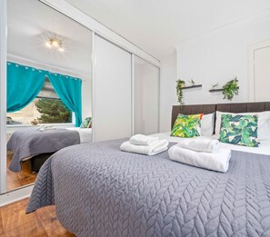 Two single beds with grey bedding and matching pillows, a large mirror, and a bedside table with a lamp.