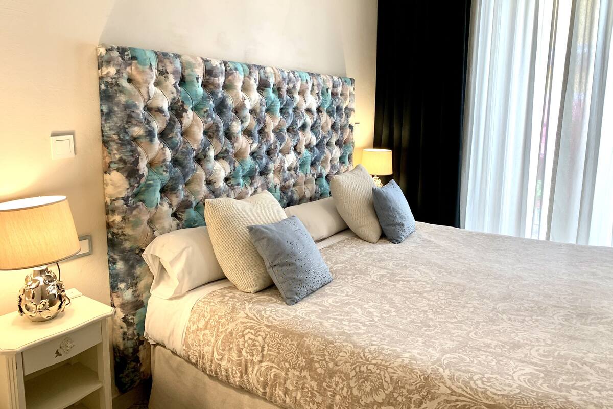 A neatly made bed with a patterned bedspread, a tufted headboard, and two bedside lamps.