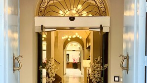 A hotel lobby with a grand arched entrance, a chandelier, and white floral arrangements.
