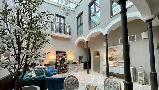 A spacious atrium with a high ceiling, a central seating area with a glass table, and a large tree with white flowers.