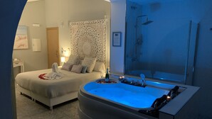 A bedroom with a large bathtub, a bed with decorative pillows, and a shower area.