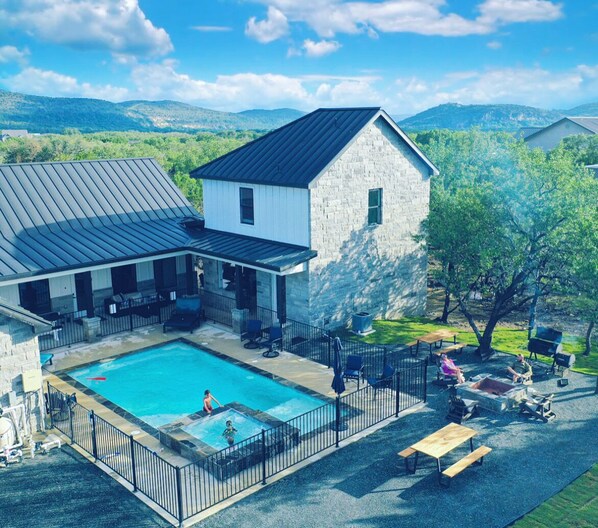 A pool area with a stone building, outdoor seating, and a view of the surrounding landscape. - Pool Spa Golf Golden Tee Sleeps 25 (Concan)