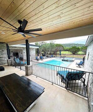 A covered outdoor area with a pool, lounge chairs, and a ceiling fan.