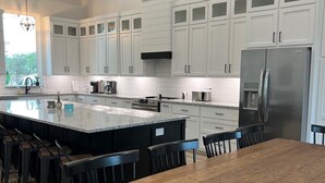 Een moderne keuken met witte kasten, een groot eiland met barstoelen, een roestvrijstalen koelkast en een houten eettafel.