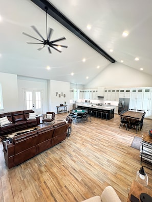 A spacious living area with a large brown leather sofa, a wooden dining table, and a kitchen area with white cabinets and a black countertop.