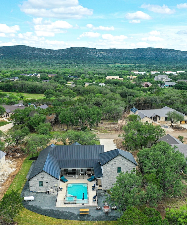 A large house with a swimming pool, surrounded by trees and hills.