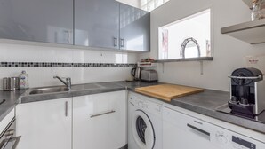 Een moderne keuken met grijze kastjes, een ingebouwde wasmachine, een koffiezetapparaat en een raam met uitzicht.