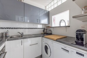 A modern kitchen with grey cabinets, a built-in washing machine, a coffee maker, and a window with a view.