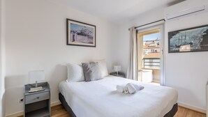 Een hotelkamer met een bed, een nachtkastje, een lamp, een ingelijste foto aan de muur en een raam met uitzicht.