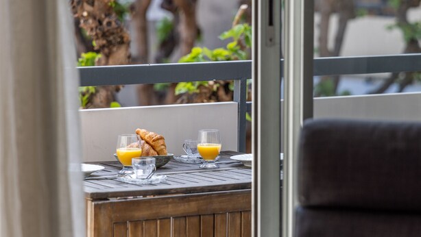 Een ontbijttafel met croissants en sinaasappelsap, een stoel en uitzicht op bomen en een gebouw.
