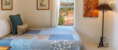 A bedroom with a large bed, a window with a view, a lamp, and two framed pictures on the wall.
