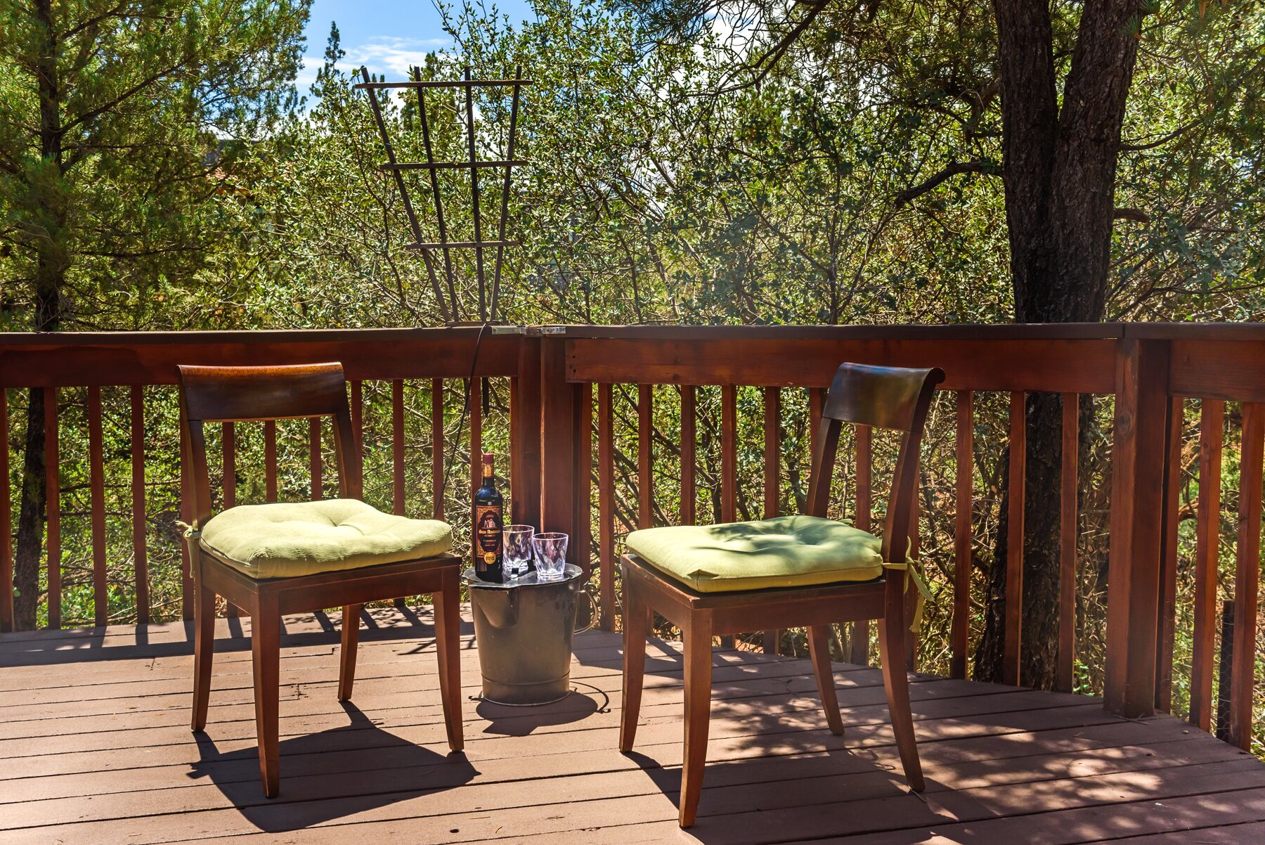 A wooden deck with two chairs and a metal table, surrounded by trees.
