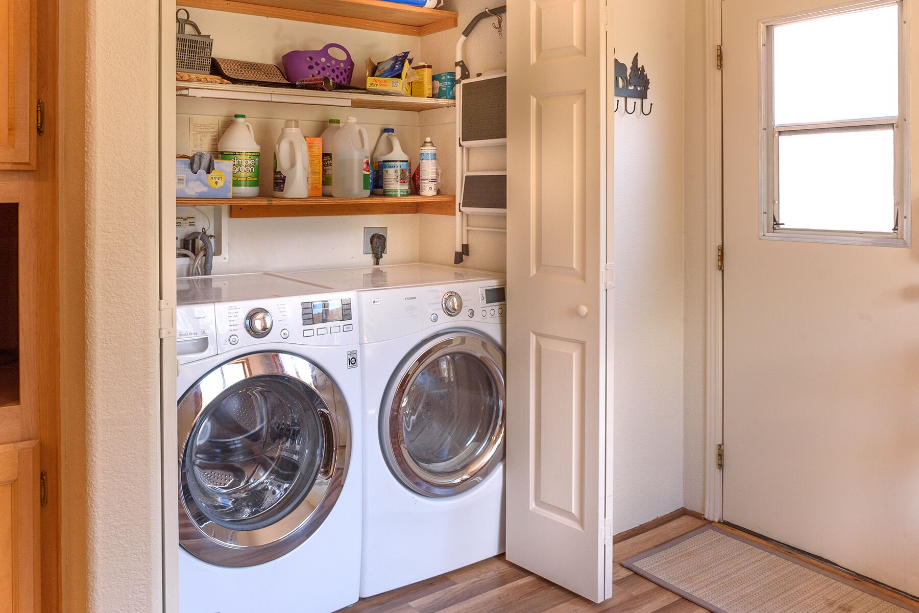 A compact laundry room with two front-loading washing machines, a shelf with cleaning supplies, and a small window.