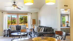 Ein gemütliches Wohnzimmer mit einer Couch, einem Couchtisch und einer großen Schüssel. Ein Fenster bietet Blick ins Freie.