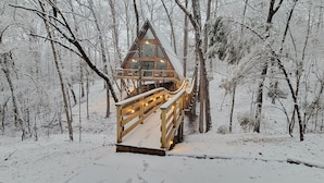 A wooden cabin with a balcony, surrounded by a snowy forest.