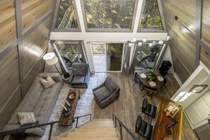 A spacious loft with a high ceiling, large windows, a staircase, and a cozy seating area with a fireplace. - The Bridge House Rock Hot Tub Buffalo River (Saint Joe)