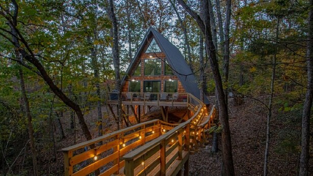 A cabin with a wooden deck and a covered area, surrounded by trees.