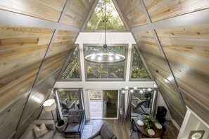 A high-ceilinged room with wooden walls and large windows, a central chandelier, and a dining area with a table and chairs. - The Bridge House Rock Hot Tub Buffalo River (Saint Joe)