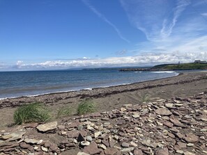 A rocky beach with a view of the ocean and distant hills.