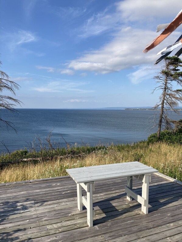 A wooden deck with a white table and benches overlooking a body of water.