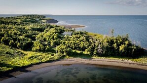 Una propiedad costera con una casa rodeada de abundante vegetación, una playa y vistas al mar.