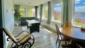 Una habitación amplia con mesa de billar, una mesa de comedor con sillas y ventanas grandes que ofrecen vistas al exterior.