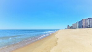 A beach with clear blue water and a sandy shore. There are high-rise buildings in the background. - Oceanfront 1 Bedroom, Balcony, Sitting Room, Pool (Ocean City)