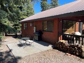 Une cabane en bois avec un patio, un barbecue et une pile de bois de chauffage.