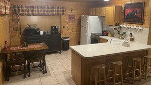 Eine gemütliche Küchenzeile im Blockhausstil mit Holzwänden, einer zentralen Kochinsel mit Barhocker, einem Kühlschrank, einer Kaffeemaschine und einem Spülbecken.