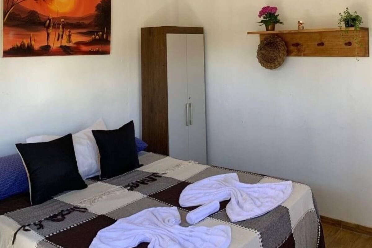 A bedroom with a bed, pillows, a quilt, a wardrobe, and a shelf with flowers.