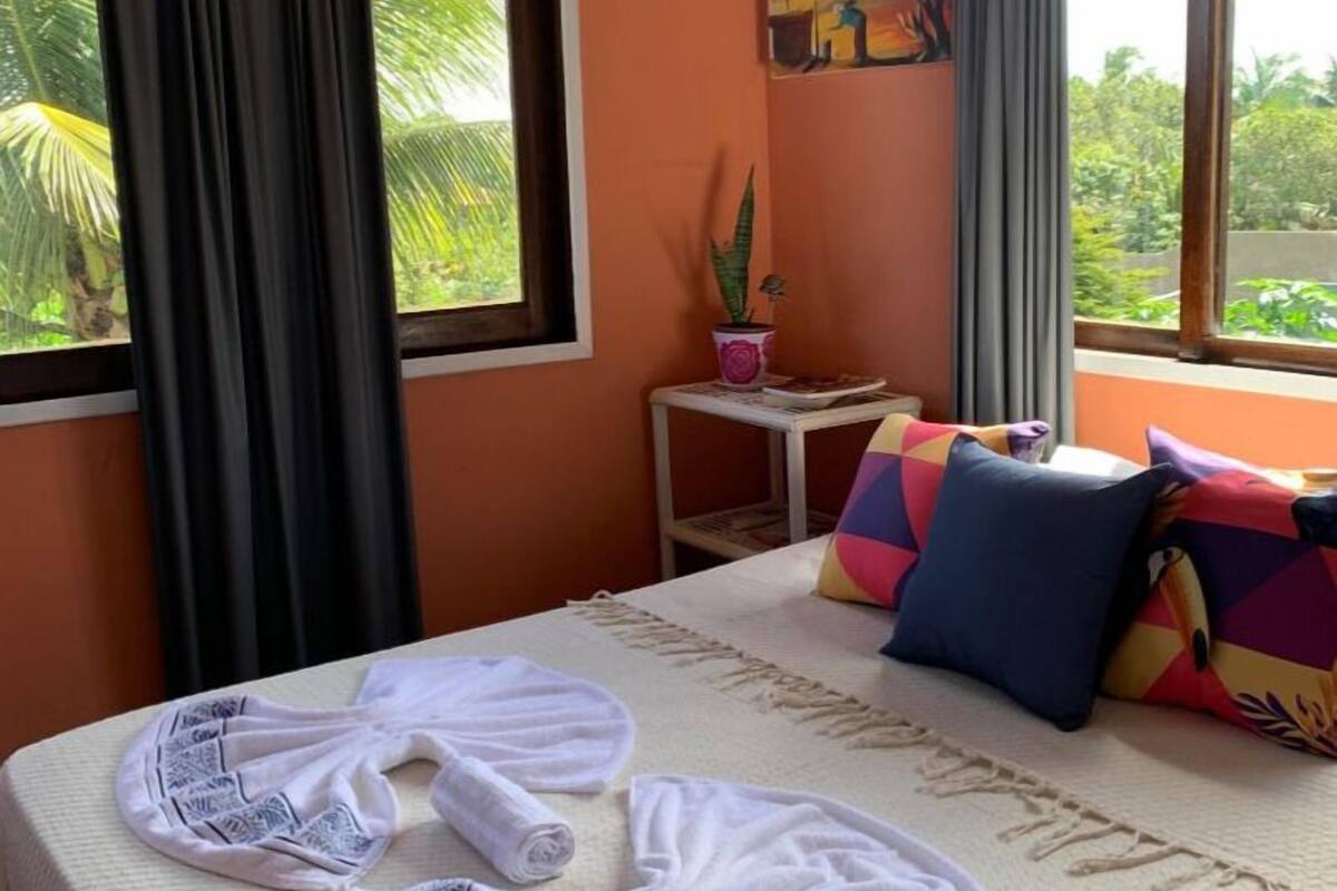 A hotel room with a bed, a small table with a potted plant, and a window with curtains.