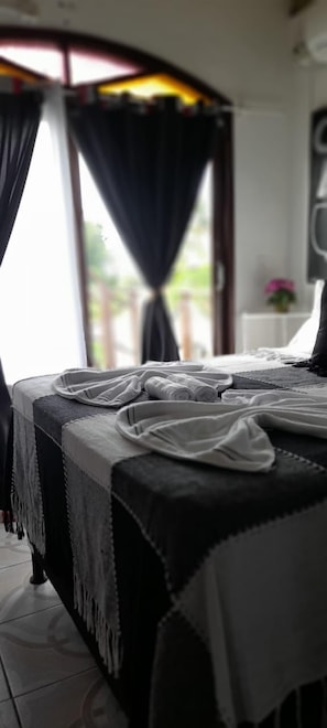 A bed with a black and white bedspread, a small table with a lamp, and a window with curtains. - A Arca Pousada (Tibau do Sul)