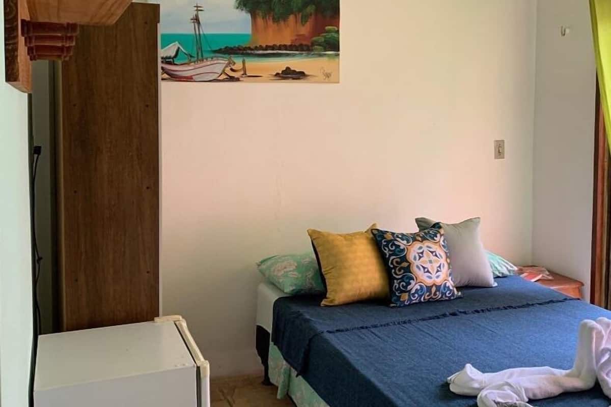 A bedroom with a bed, pillows, a small table, and a painting of a beach scene on the wall.