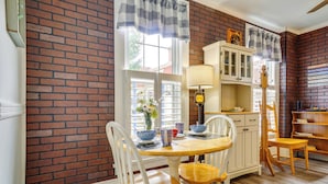 A dining area with a brick wall, white chairs, a wooden table, and a cabinet with glass doors. - Quaint Mt Vernon Cottage Near Historic Dtwn! (Mt Vernon)