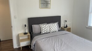 Un dormitorio con cama, mesita de noche, lámpara de pared y una cita enmarcada en la pared.
