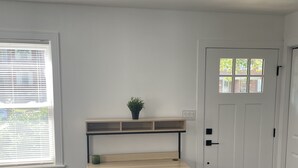 Una habitación con un escritorio de madera, una silla blanca, una planta pequeña y una puerta con un ventanal.
