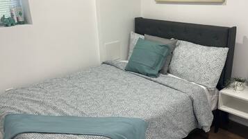 A neatly made bed with patterned bedding, a bedside table with a lamp, and a wall-mounted abstract painting.